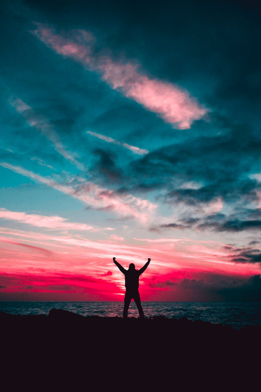 Silhouette of man raising hands against a red sunset. In our final key beat, the hero finds a way through the darkness: one last chance to persevere.