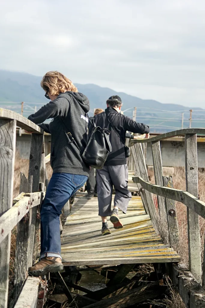 People crossing a broken wooden bridge.