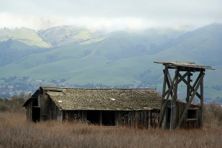 Hills rise behind a shack and the remains of a water tower.