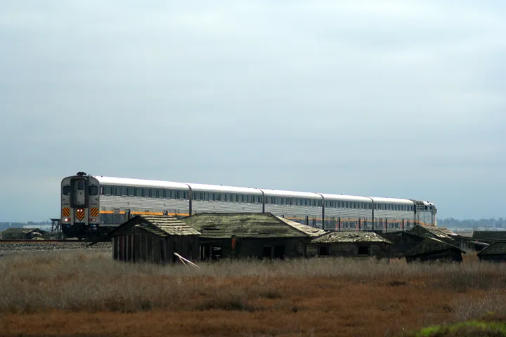 A freight train passes a set of shacks.