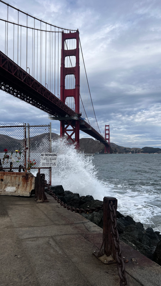 Golden Gate Bridge seen from Fort Point with waves crashing against the shore.