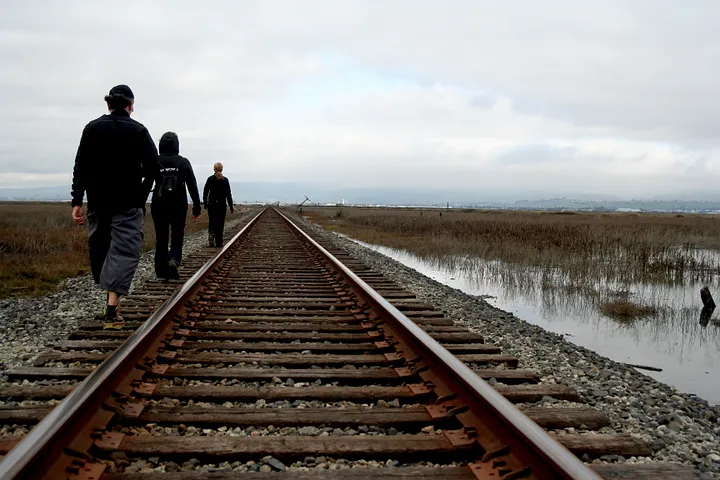 People walking alongside a train track towards Drawbridge, CA.