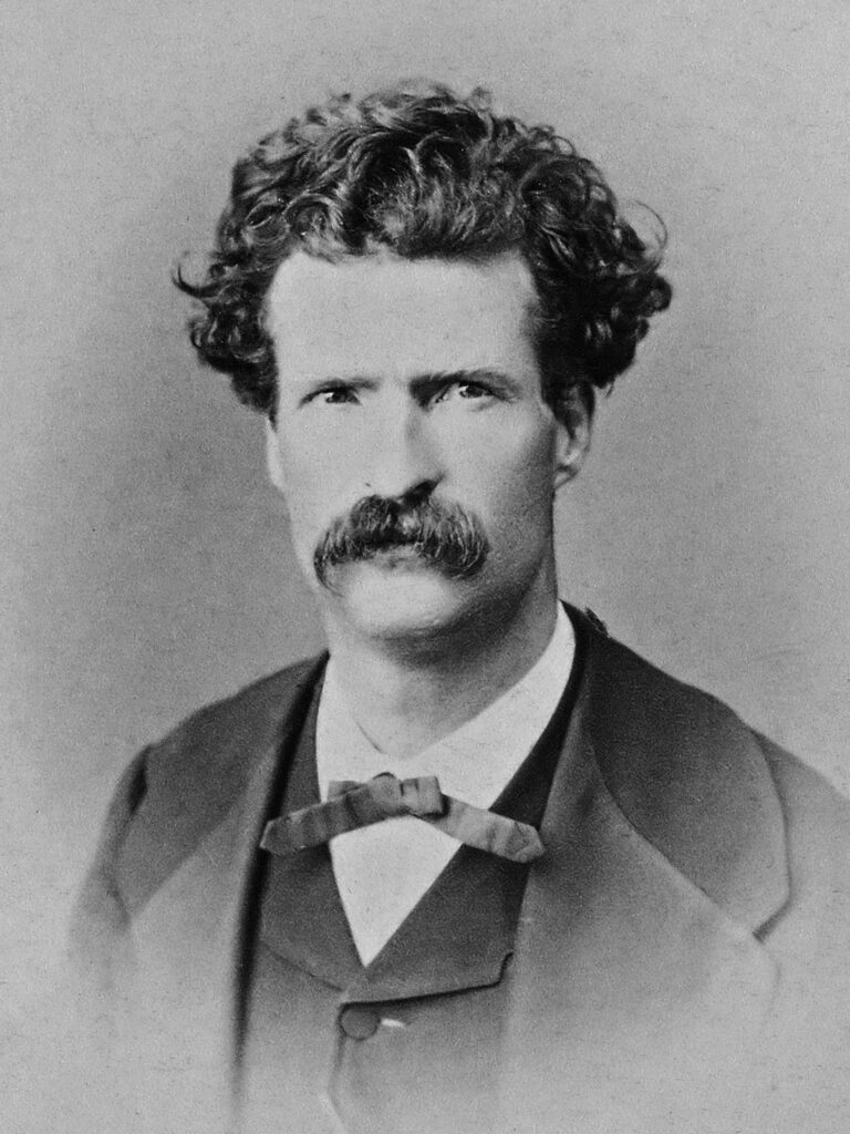 Photo of Mark Twain, aged 32. He sports curly hair, a heavy mustache and a thin bow tie.