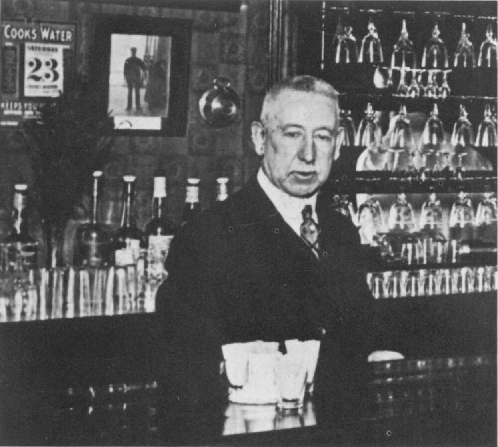 Black and white photo shows an older man behind a bar.