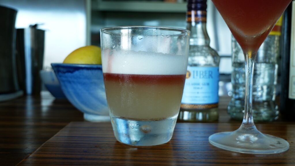 A layered cocktail, white on top, deep red in the middle, and pale green at the bottom.