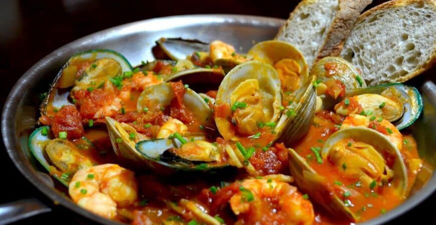 A stew of mussels and clams in a metal bowl.